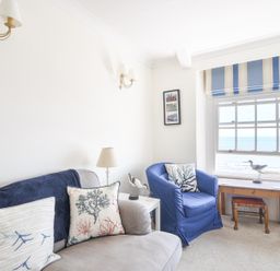 A sitting room with a gray sofa and blue armchair near a window overlooking the sea at 3 Argyle House in Lyme Regis