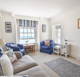 A living room with blue armchairs a beige sofa and a window with a sea view at 3 Argyle House in Lyme Regis