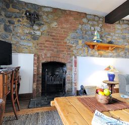 A living room with stone and brick walls a wooden table with fruit and a television on a desk at Bedrock in Lyme Regis
