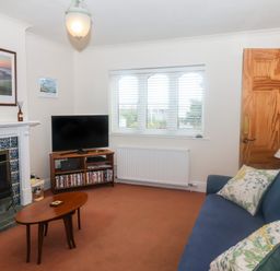 A living room with a blue sofa a wooden coffee table a television on a stand and a fireplace at 2 Kersbrook Gardens Lyme Regis