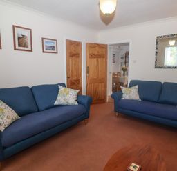 A living room with two blue sofas and wooden doors at 2 Kersbrook Gardens in Lyme Regis