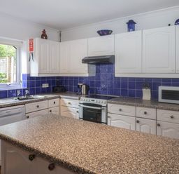 A kitchen with white cabinets blue tile backsplash and speckled countertops at 2 Kersbrook Gardens Lyme Regis