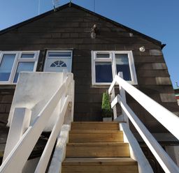 Wooden stairs with white railings leading to a door and windows on the upper floor of a dark shingled building at 11 The Gables in Lyme Regis