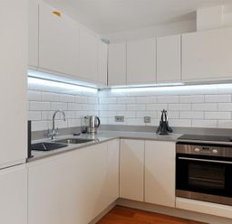 A kitchen with white cabinets a built in oven a kettle and utensils on the counter at The Lower Deck in Lyme Regis