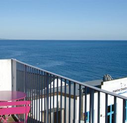 A balcony with pink table and chairs overlooking the ocean and a marine theatre building at 9 Bay View Court in Lyme Regis