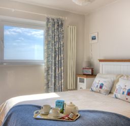A bedroom with a bed and breakfast tray next to a window with sea view at 9 Bay View Court Lyme Regis