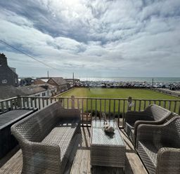 A balcony with chairs and a table overlooking the sea at 8 Bowling Green Chalets in Lyme Regis