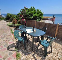 An outdoor patio area with a plastic table and four chairs on gravel next to a stone pathway overlooking the sea at Ross House Lyme Regis