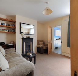 A living room with a beige sofa and armchair a black fireplace and shelves with books at 23 Lym Close in Lyme Regis