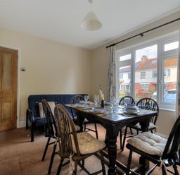 A dining room with a wooden table set for six and a sofa near a window at 23 Lym Close in Lyme Regis