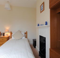 A bedroom with two single beds a wooden nightstand a lamp a fireplace and shelving at 23 Lym Close Lyme Regis