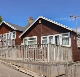 A wooden house with a fenced porch and outdoor seating under a clear blue sky at Granny's Teeth in Lyme Regis