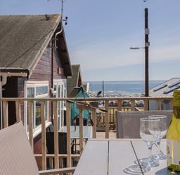 A balcony with a table holding a bottle of wine and two wine glasses overlooking houses and the sea at Grannys Teeth in Lyme Regis