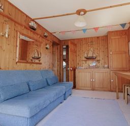A room with wooden paneled walls a blue sofa a wooden cabinet model sailboats on walls and a wooden table with stools at Granny's Teeth Lyme Regis