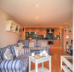 A living room with blue striped sofas and pillows and a kitchen with wooden cabinets and blue tile backsplash at 2 Buckfields in Lyme Regis