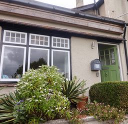 The exterior of a house with a green door and windows with plants and shrubs in front at The Apartment at Queen Anne's Lodge in Lyme Regis