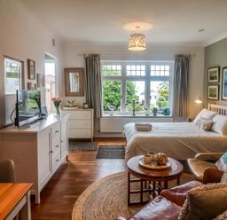 A bedroom with a bed a TV on a cabinet and a table with chairs at The Apartment at Queen Anne's Lodge in Lyme Regis