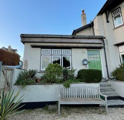 Front of a house with a green door, windows, plants, and a wooden bench in the garden at The Apartment at Queen Anne's Lodge in Lyme Regis