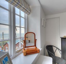 A room with a large window showing a seaside view a wooden mirror on the windowsill a black woven chair and a fireplace at 10 Cobb Terrace in Lyme Regis