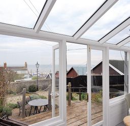 A conservatory with glass roof and white frames overlooking a garden with outdoor table and bench at 10 Cobb Terrace in Lyme Regis