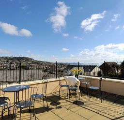An outdoor terrace with black metal tables and chairs overlooking houses and hills at Jurassic Sea View in Lyme Regis