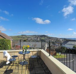 A balcony with a table and chairs overlooking a residential area and hills at Jurassic Sea View Lyme Regis