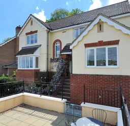 An outdoor patio with chairs and a table in front of a two story house with cream and brick exterior Jurassic Sea View Lyme Regis