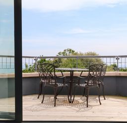 A balcony with a metal table and four metal chairs overlooking trees and water at The Penthouse in Lyme Regis
