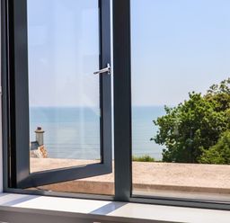 A window open showing a view of the sea trees and a rooftop at The Penthouse in Lyme Regis