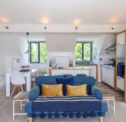 A living room with a blue sofa a dining table and an open kitchen at The Penthouse in Lyme Regis