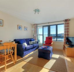 A living room with a blue sofa red chair wooden dining table and a television at 8 Driftwood in West Bay