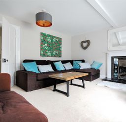 A living room with a brown sectional sofa and blue pillows a wooden coffee table a fireplace with a mirror above it and wall art at Mermaid House in Lyme Regis