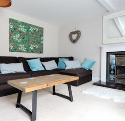A living room with a dark sofa with blue and white cushions a wooden coffee table a fireplace with decorative tiles and a mirror above it and a heart shaped wall decoration at Mermaid House in Lyme Regis