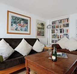 A living room with brown sofas white cushions a wooden table a bookshelf and paintings at 24 Mill Green Lyme Regis