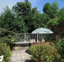 A garden patio with a table chairs and a striped umbrella surrounded by plants at 24 Mill Green Lyme Regis