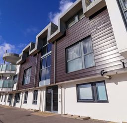 Exterior of a modern apartment building with glass balconies and wooden paneling at 2 Driftwood in West Bay