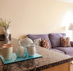 A kitchen counter with tea set and mugs with a purple sofa and patterned cushions in the background at 2 Driftwood in West Bay