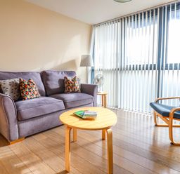 A living room with a purple sofa and patterned cushions a round wooden coffee table and a blue armchair with a cushion at 2 Driftwood in West Bay