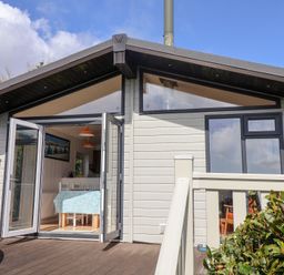 A small lodge with an open door leading to a dining area with a table and chairs on a wooden deck at High Bullen Lodge in Morcombelake