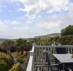 A balcony with a table and chairs overlooking a garden and countryside with a view of the sea at High Bullen Lodge in Morcombelake