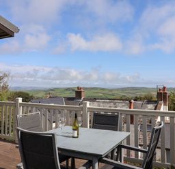 A balcony with a table and four chairs overlooking rooftops and green hills at High Bullen Lodge in Morcombelake
