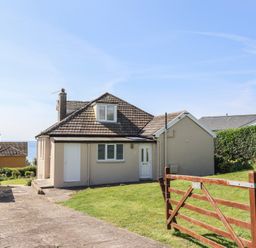 A house with a tiled roof a driveway and a wooden gate with grass lawn at Tillicum in Charmouth