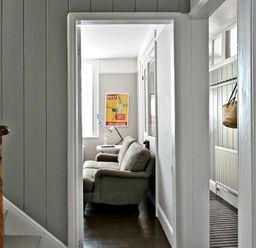 A hallway with a staircase and doorway leading to a room with a sofa and side table with a lamp at The Arched House in Lyme Regis