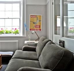 A sitting area with a gray sofa a side table with a lamp a window with flowers and a framed poster on the wall at The Arched House in Lyme Regis