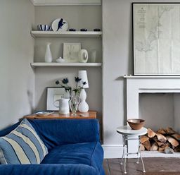 A living room with a blue sofa and shelves above a wooden side table next to a fireplace with firewood at The Arched House in Lyme Regis