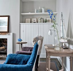 A sitting room with armchairs a fireplace a wooden table with a glass vase and a model sailboat at The Arched House in Lyme Regis