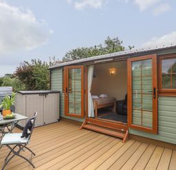 An outdoor deck with table, chairs, storage box, and open door to a small room at Llety'r Bugail 2 in Llanrug