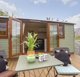 An outdoor patio with table and chairs in front of a small cabin with open double doors at Llety'r Bugail 2 in Llanrug