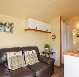 A small living area with a brown leather sofa and cushions next to a kitchen countertop at Llety'r Bugail 2 in Llanrug