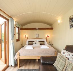 A bedroom with a wooden bed and brown pillows next to a brown leather sofa with cushions at Llety'r Bugail 2 in Llanrug